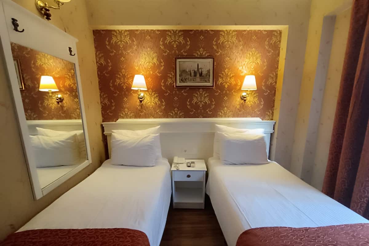 A hotel room with two single beds, a nightstand, a mirror, and a wall-mounted picture.