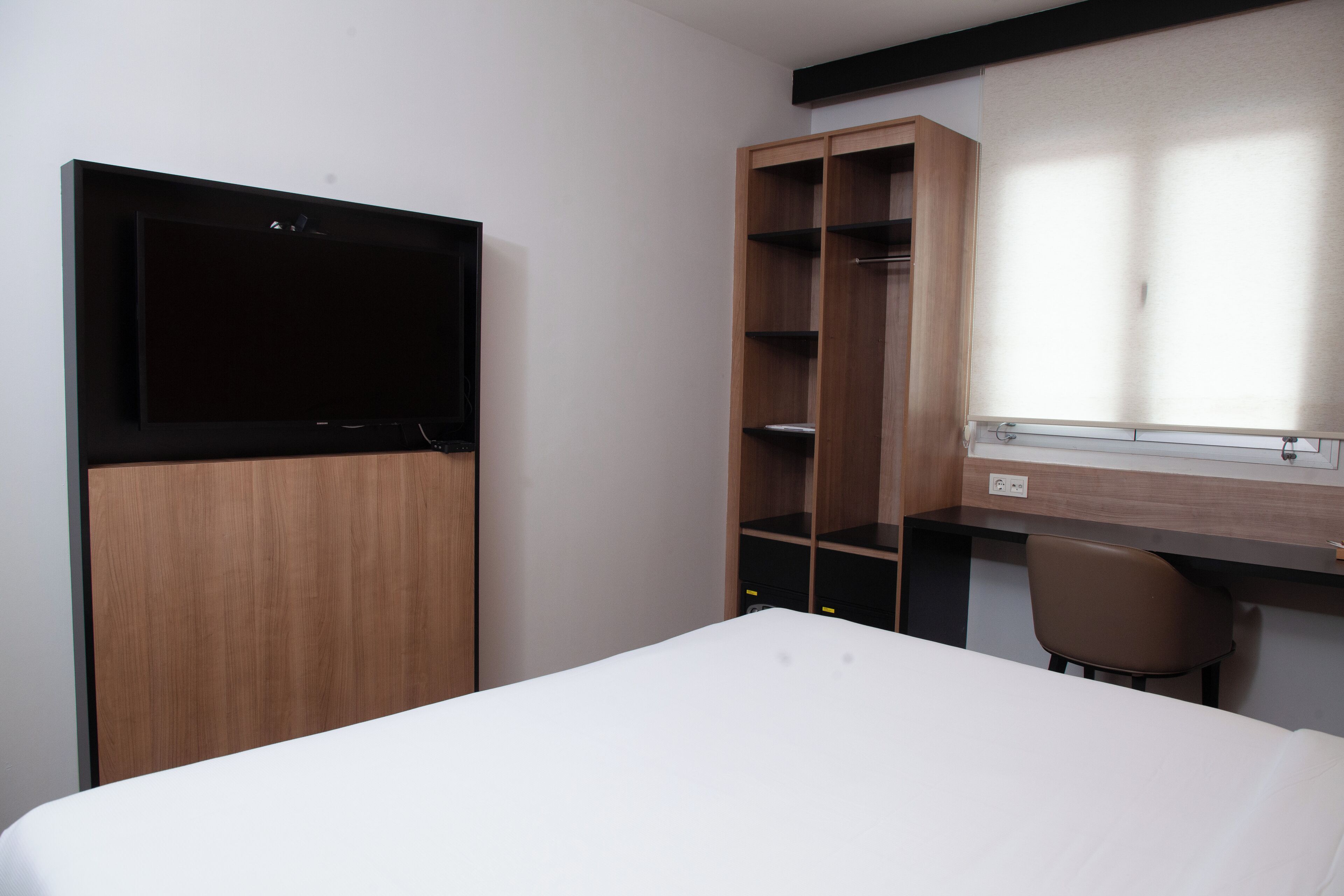 A hotel room with a bed, a desk, a chair, and a wardrobe.