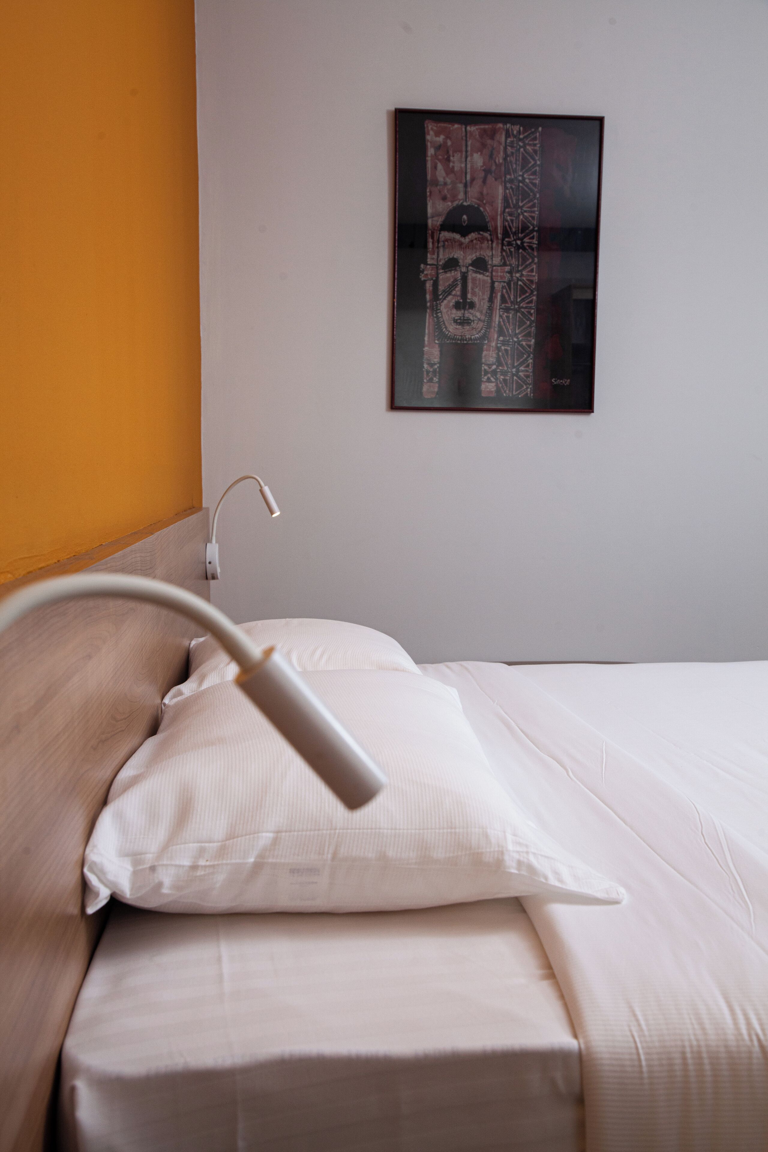 A neatly made bed with white linens, a white bedside lamp, and a framed artwork on the wall.
