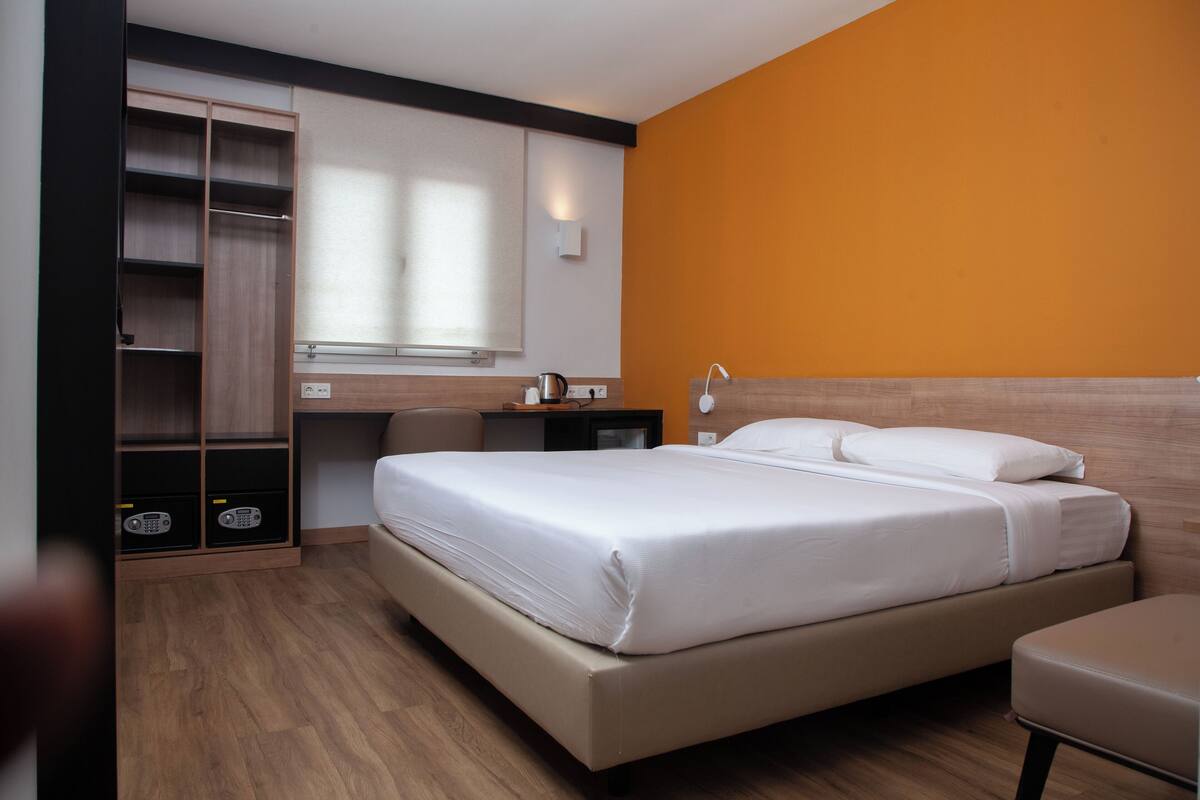 Ein Hotelzimmer mit einem großen Bett, einem Schreibtisch, einem Kleiderschrank und einem Fenster mit Jalousien.