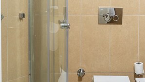 A bathroom with a glass shower enclosure, a toilet, and a towel rack with a white towel.