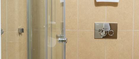 Un baño con cabina de ducha de vidrio, un inodoro y un perchero con una toalla blanca.