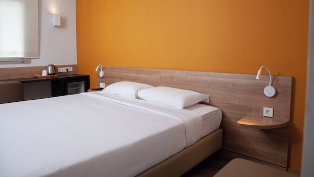 A hotel room with a bed, a nightstand, a desk, and a window with blinds.