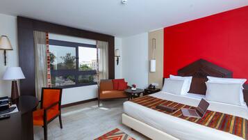 A hotel room with a bed, a desk with a chair, a small table, and a window with curtains.