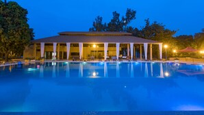 Un hotel con piscina, zona de estar exterior cubierta y un edificio con techo de tejas.