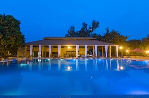 Un hotel con piscina, zona de estar exterior cubierta y un edificio con techo de tejas.