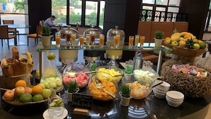 Un bufé con diversas frutas, zumos y un cartel que indica frutas frescas.