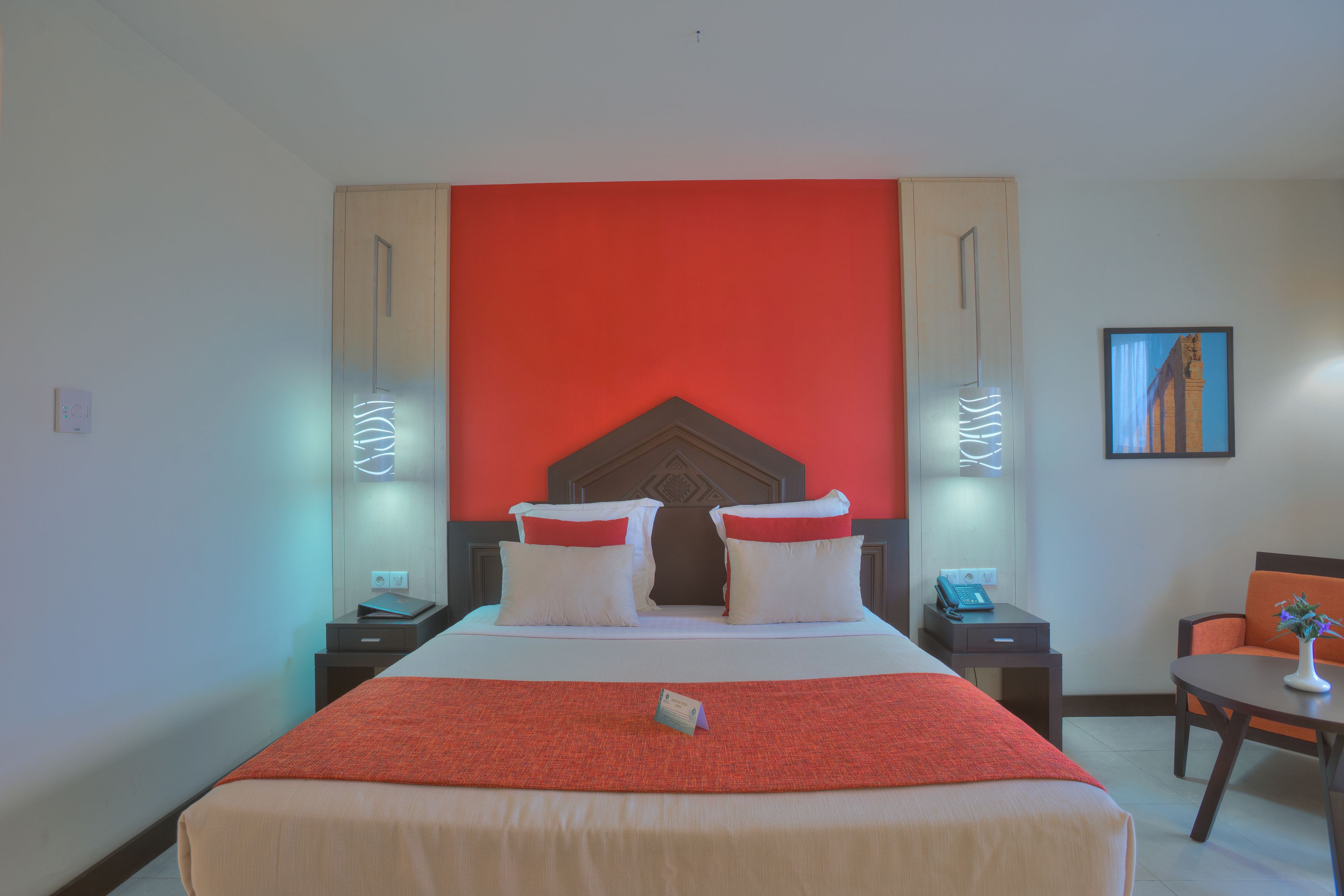 Habitación de hotel con una cama grande, dos mesitas de noche, una silla y una pequeña mesa con un florero.