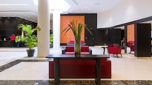 Un vestíbulo moderno con un mostrador de recepción, asientos rojos y una planta grande en maceta.