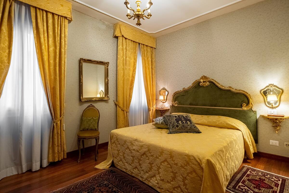 A room with a bed, a chair, a mirror, and a nightstand with a lamp.