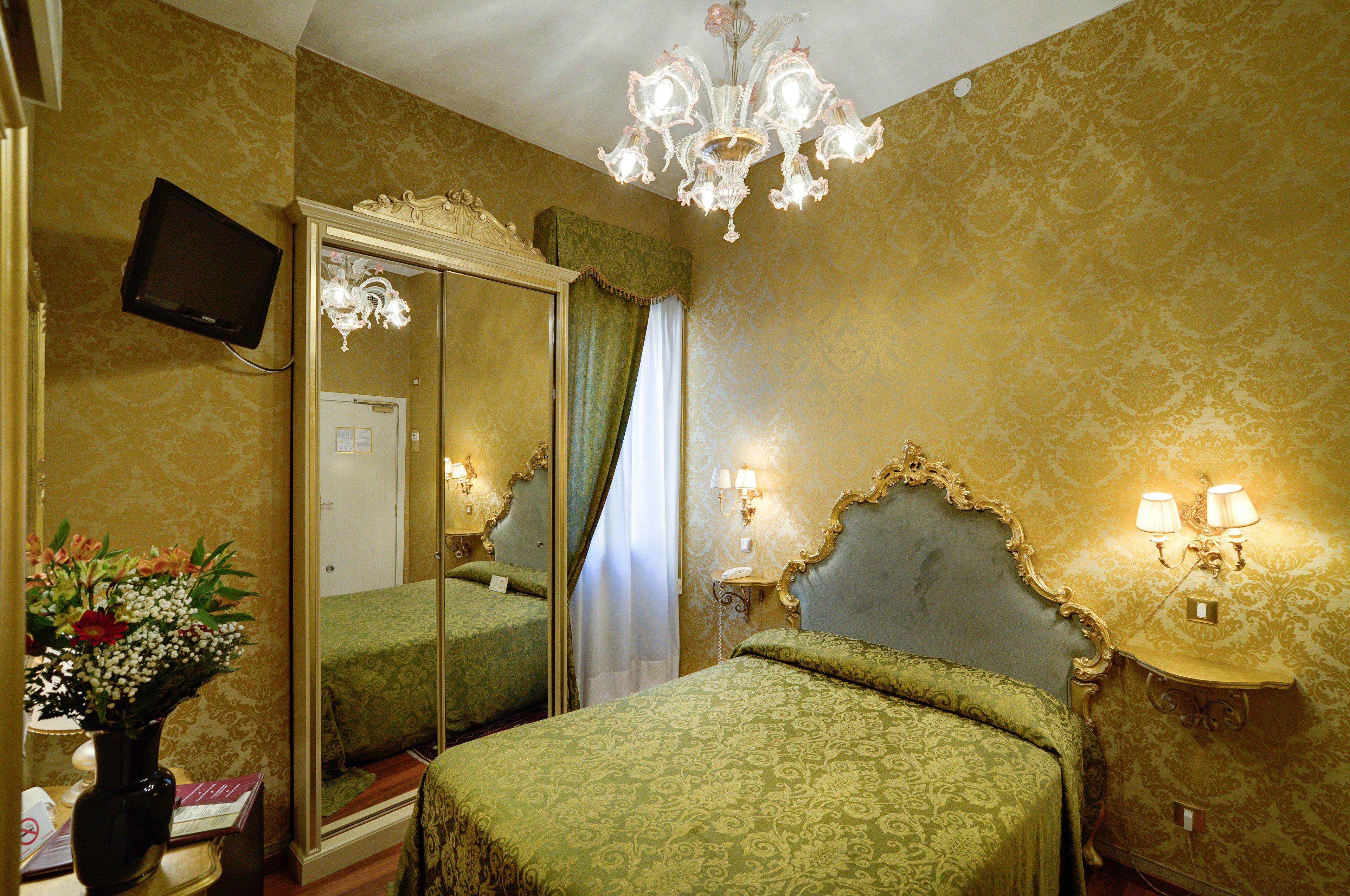 Una habitación de hotel con un espejo grande, una araña y una cama con ropa de cama verde.