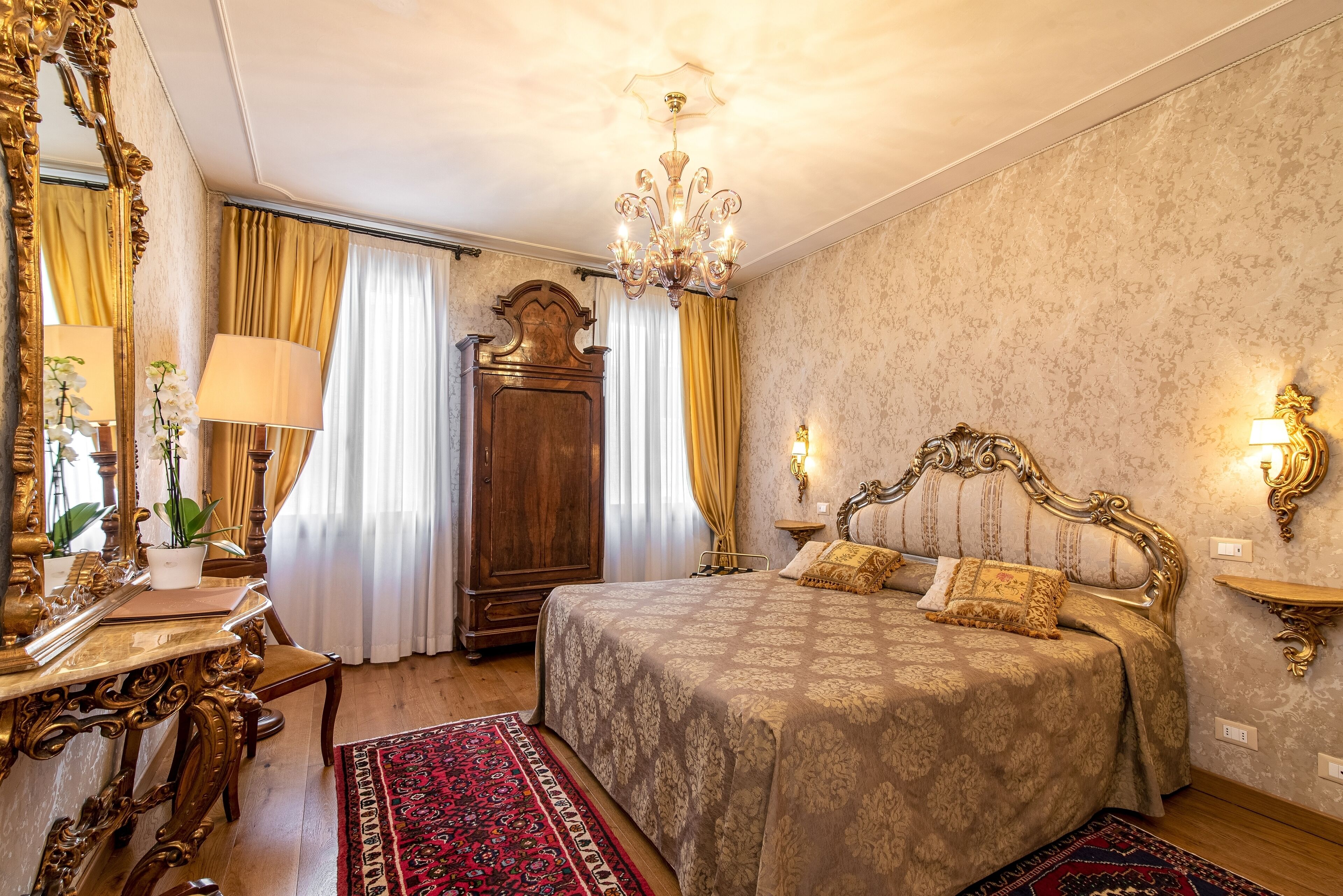 A classic, elegantly furnished bedroom with a large bed, ornate furniture, and a chandelier.