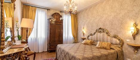 A classic, elegantly furnished bedroom with a large bed, ornate furniture, and a chandelier.