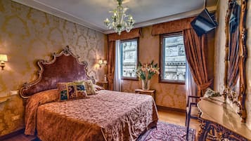 Un dormitorio lujoso con una cama grande y elaborada, un candelabro y vistas a un edificio histórico a través de las ventanas.
