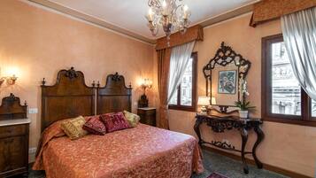 A bedroom with a large bed, a chandelier, a wooden headboard, a nightstand, a bedside table, a mirror, and a window with curtains.