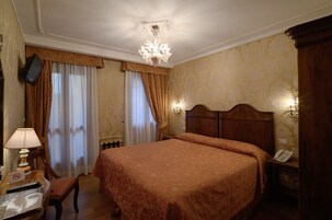 A hotel room with a large bed, a desk with a lamp, a chair, a television mounted on the wall, and a telephone on the bedside table.