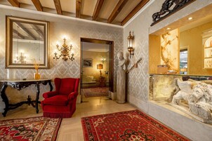 Una habitación con un sillón rojo, un espejo grande, una araña y una vitrina de cristal con esculturas.