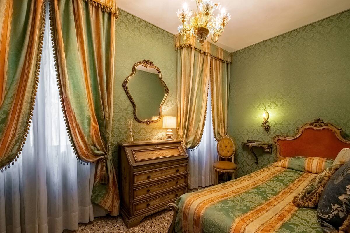 A room with a bed, a dresser, a chair, a mirror, and curtains.