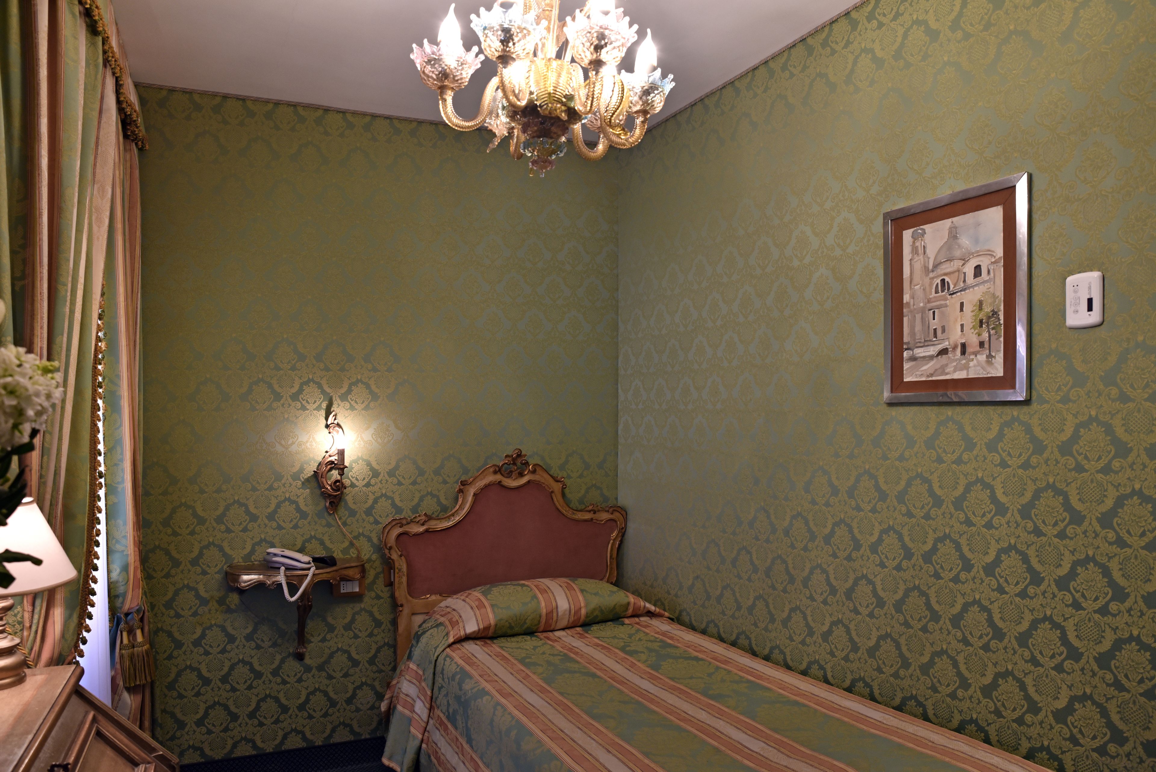 A bedroom with a bed, a chandelier, a wall-mounted light, and a framed picture.