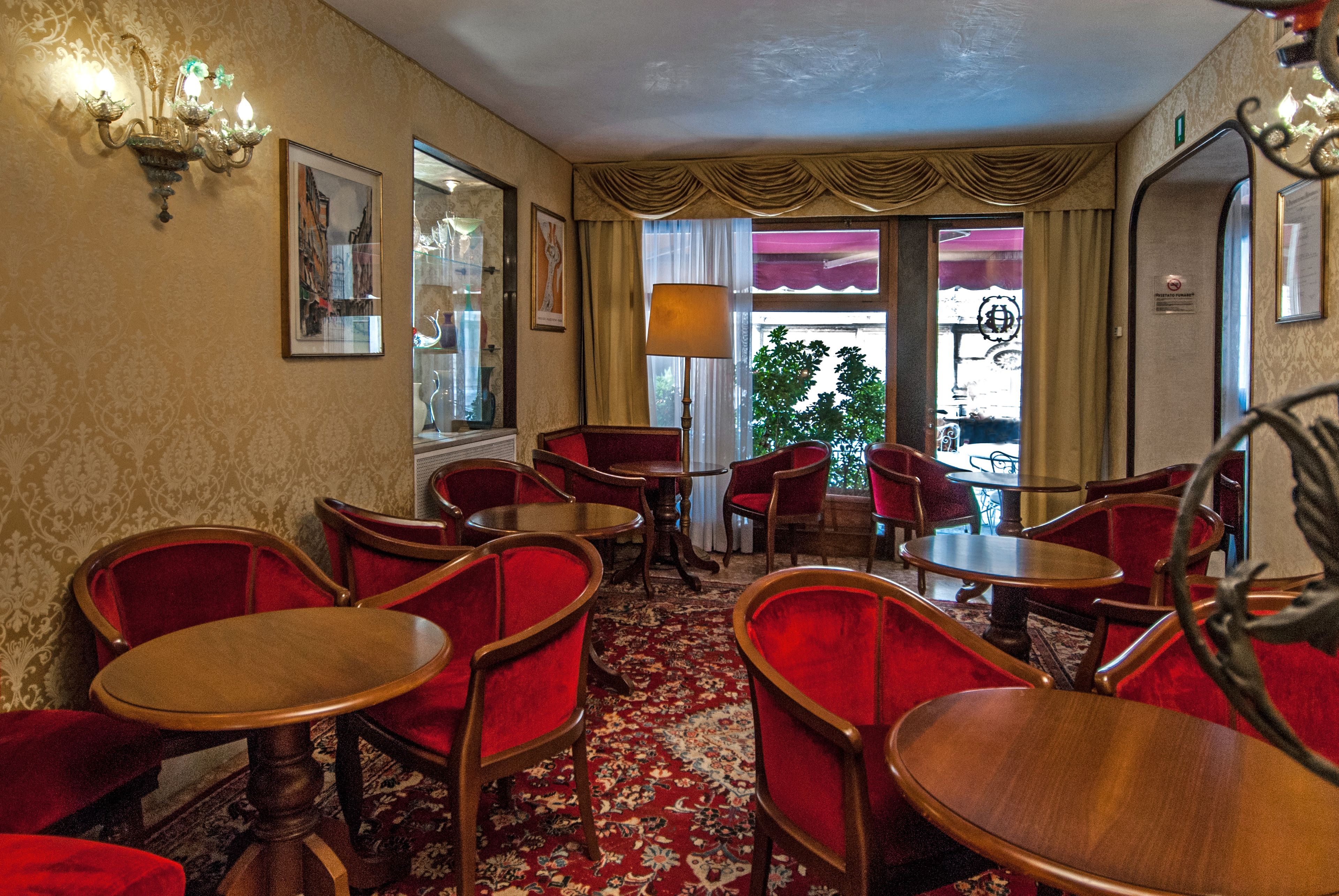 Une chambre d’hôtel avec des fauteuils à revêtement rouge, des tables en bois, une moquette à motifs et une grande fenêtre avec des rideaux.