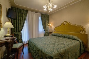 Quarto com uma cama grande, uma escrivaninha com luminária, uma televisão na parede e um candelabro.
