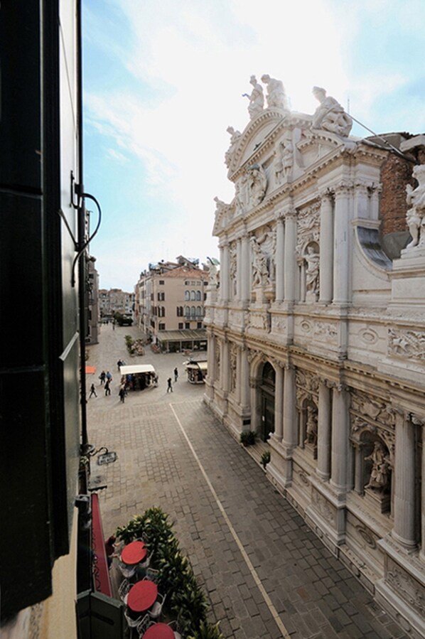 Vista de una calle con edificios ornamentales, una plaza empedrada y algunas personas caminando.