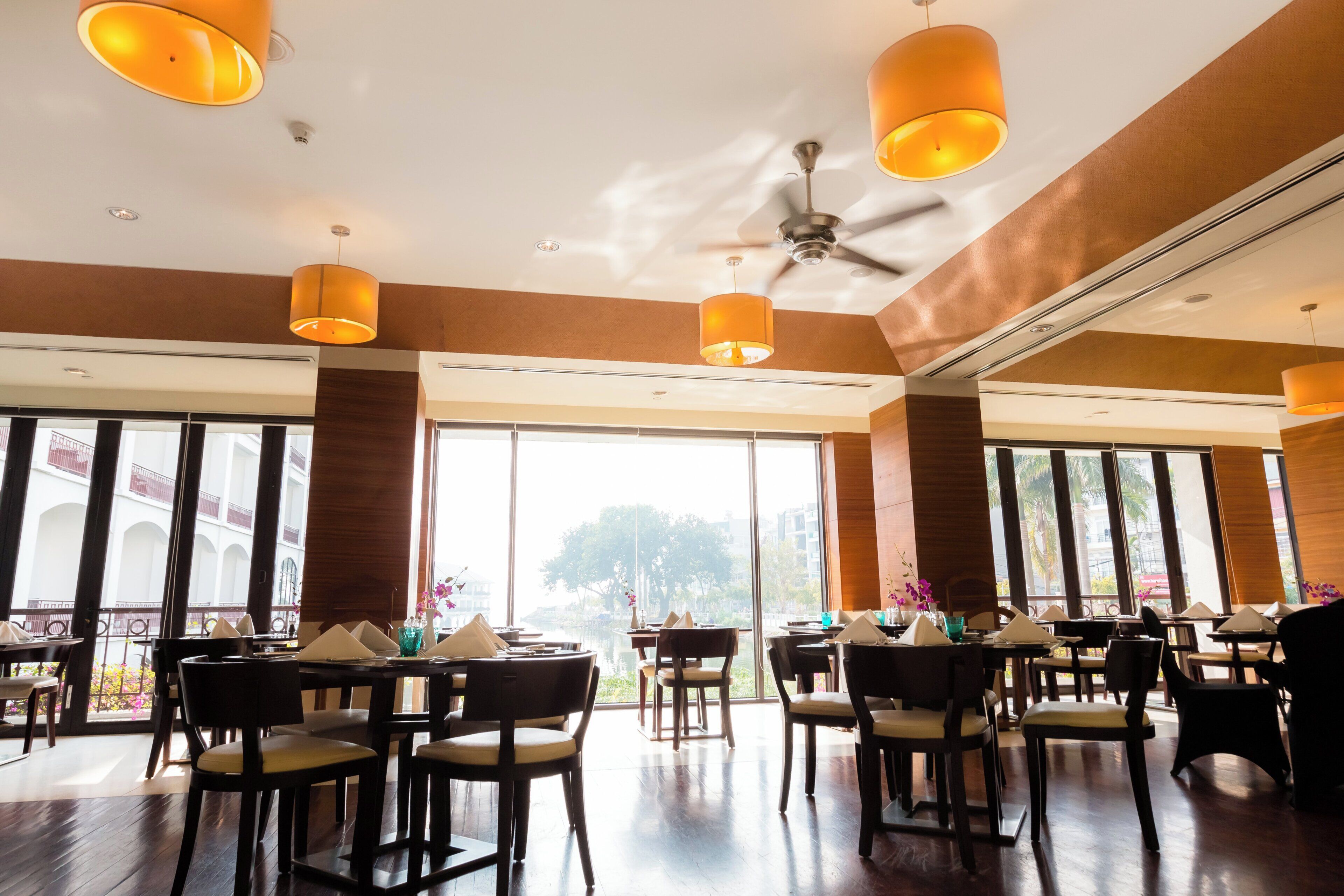 A spacious dining area with multiple tables and chairs, large windows, and ceiling fans.