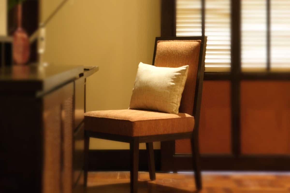 A chair with a cushion in a room with a wooden floor and a window with blinds.