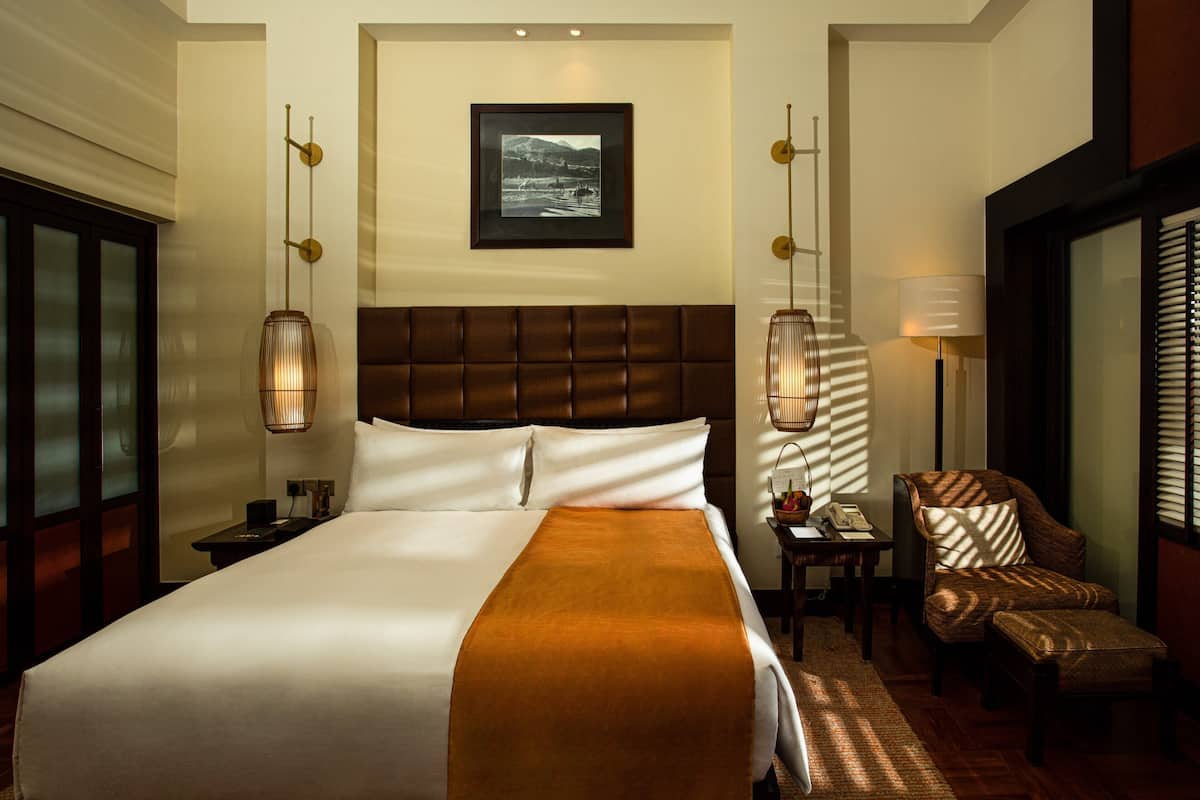 A hotel room with a large bed, a headboard, a bedside table, a lamp, a chair, and a picture on the wall.