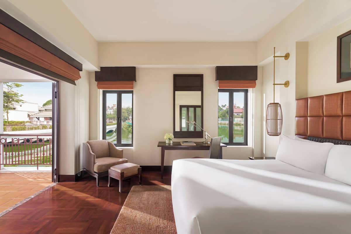 A modern hotel room with a large bed, a desk, a chair, and a balcony with a view of the city.