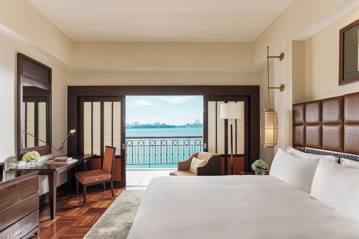 Hotelkamer met een groot bed, een bureau met stoel, uitzicht op zee en een balkon.