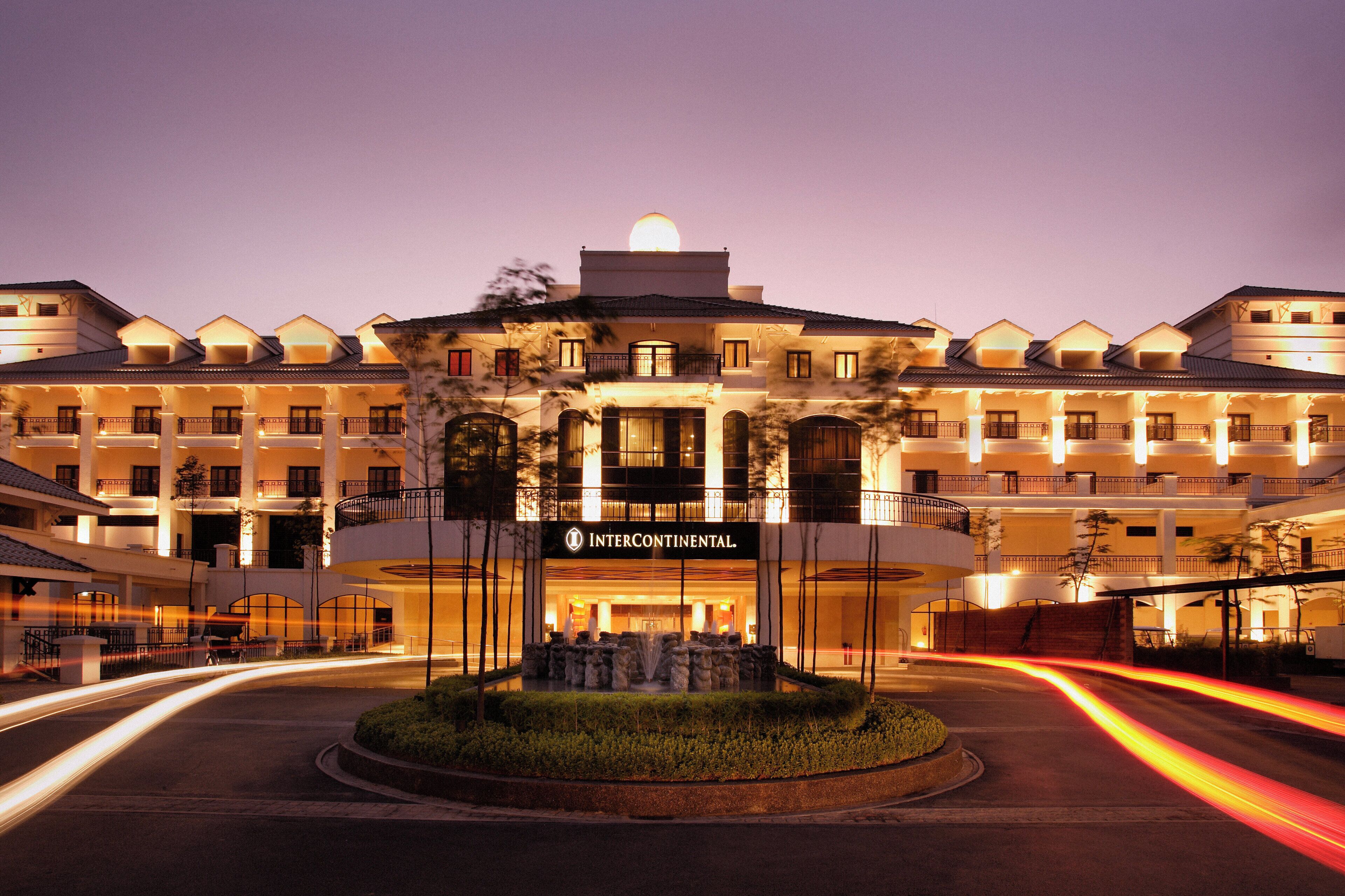 A hotel with a central entrance, multiple balconies, and a landscaped area with a fountain.