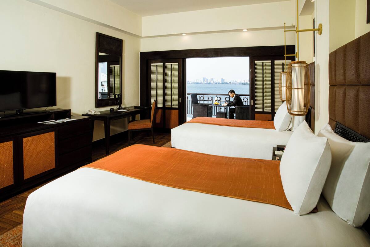 A hotel room with two beds, a desk, a television, and a view of the city.