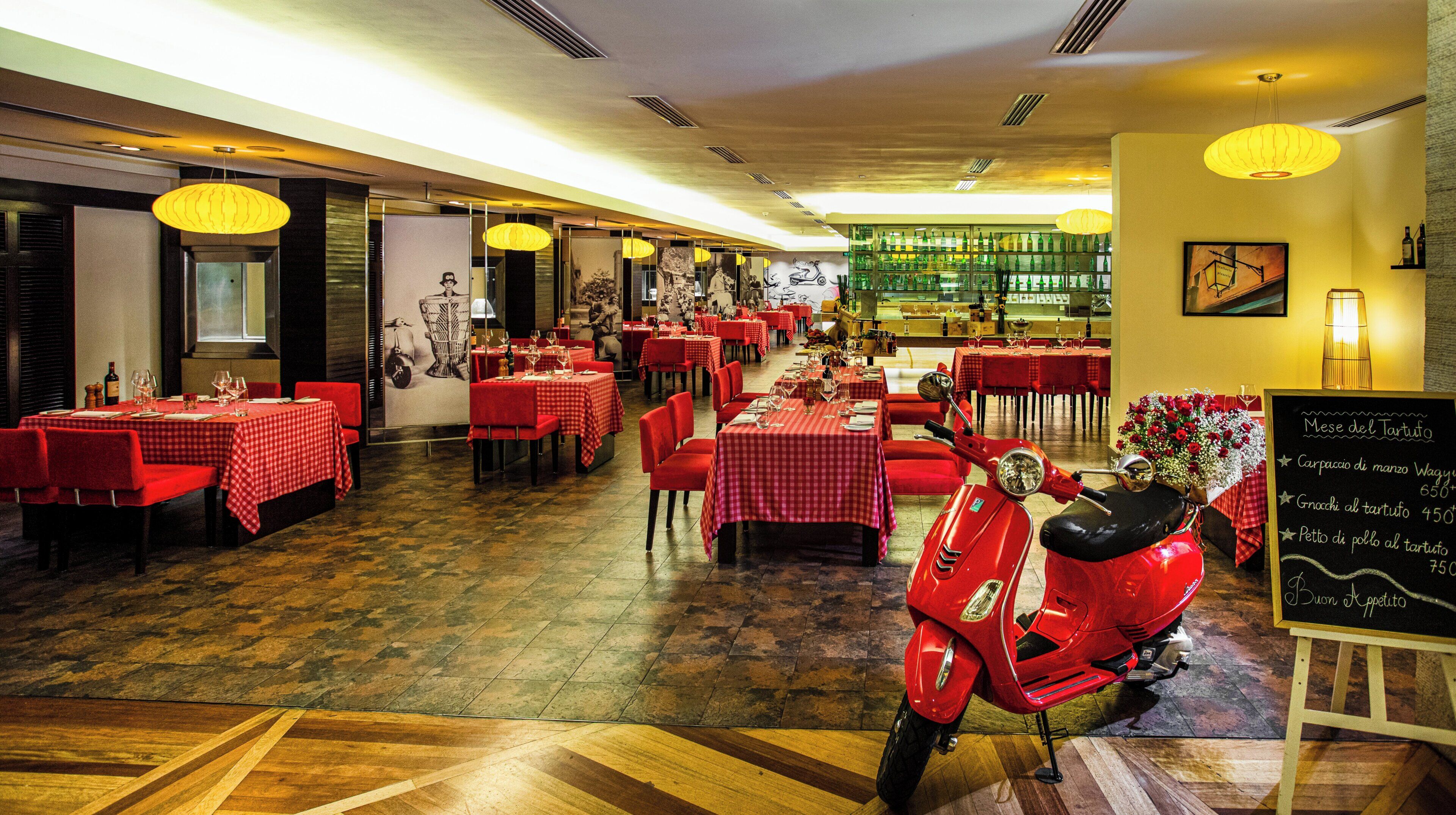 A restaurant with red checkered tables and chairs, a red scooter, and a chalkboard menu.