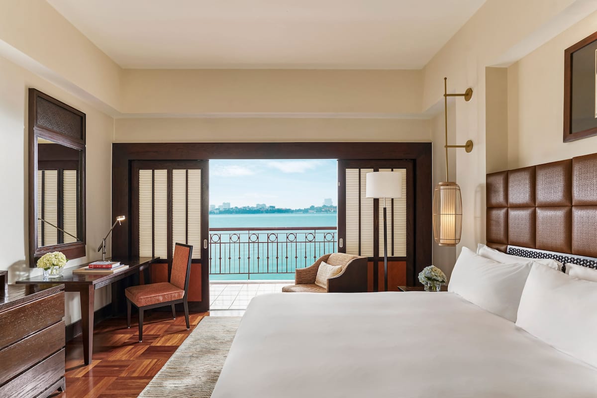 A hotel room with a large bed, a desk with a chair, a view of the sea, and a balcony.