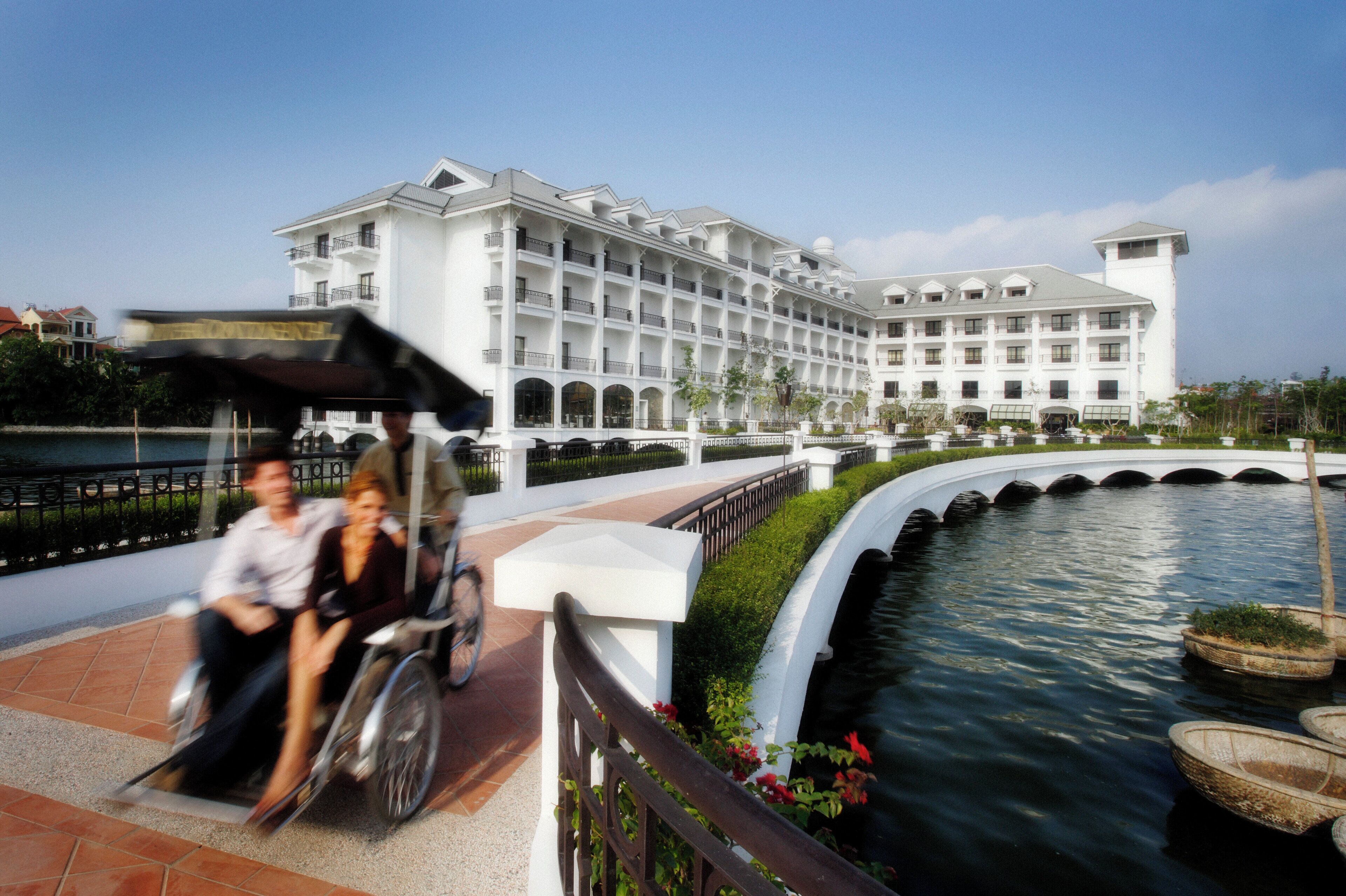 A large white hotel with multiple balconies and a water feature in the foreground.