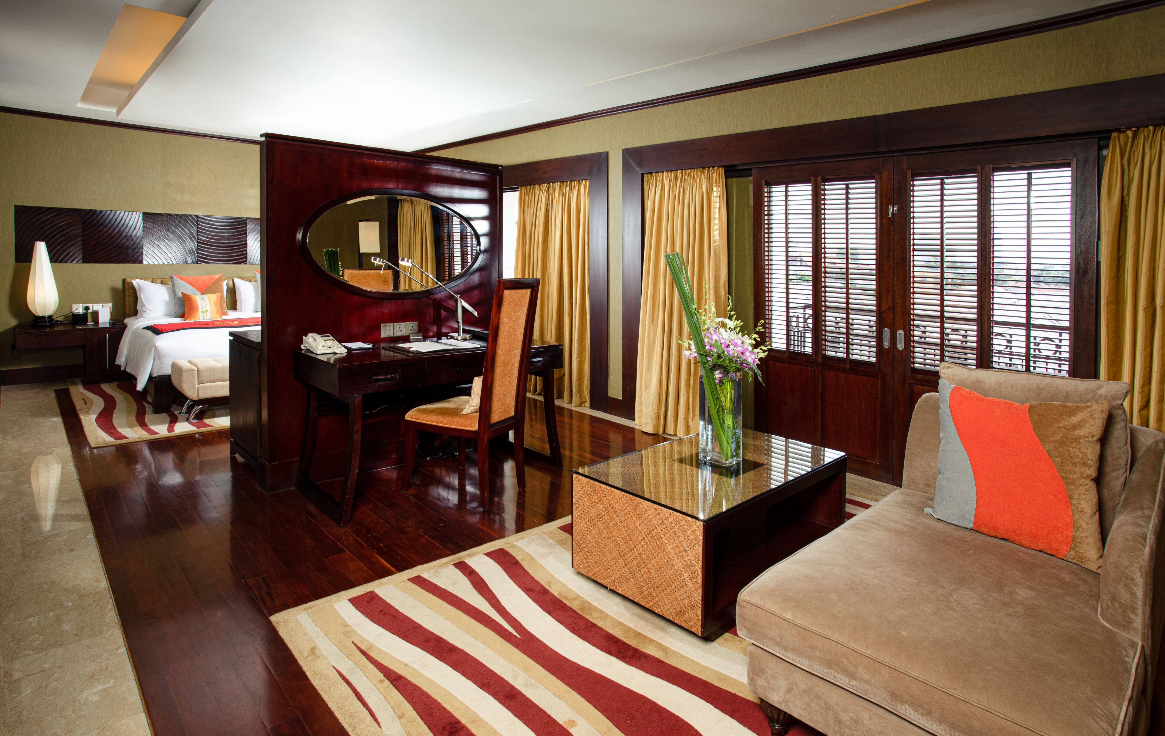 Een hotelkamer met een bed, een bureau, een stoel, een bank, een bijzettafeltje en een groot raam met gordijnen.