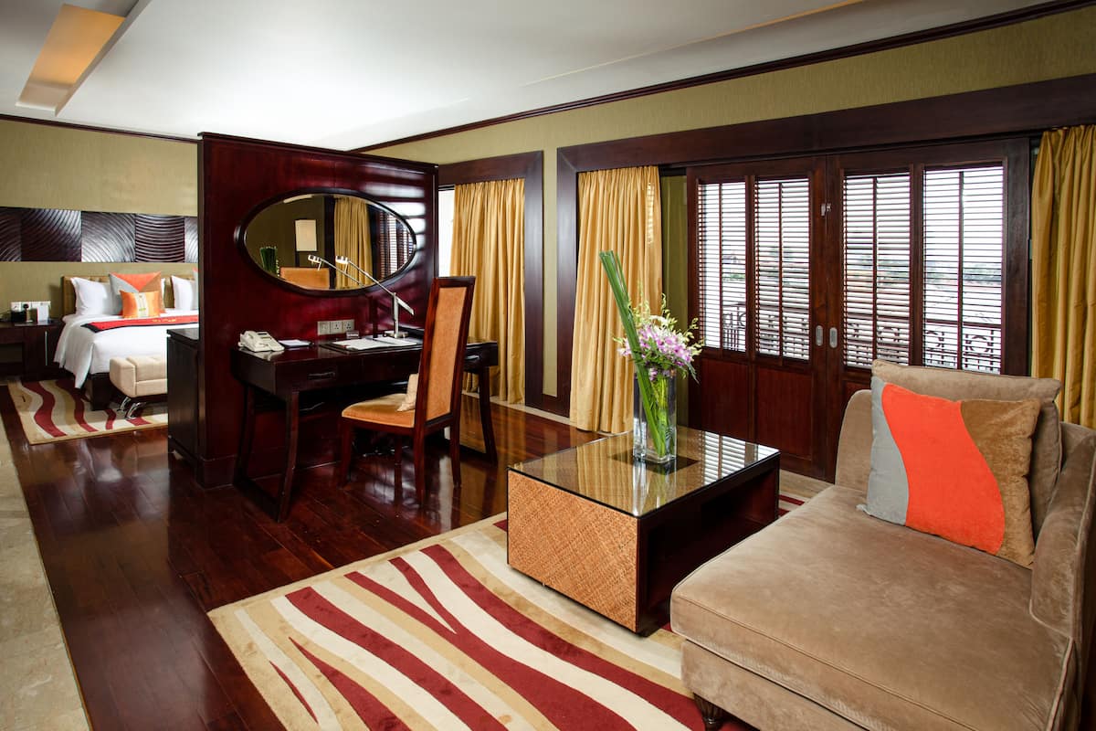 A hotel room with a bed, a desk, a chair, a sofa, a coffee table, and a large window with curtains.