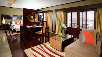 Habitación de hotel con cama, escritorio, silla, sofá, mesita de café y un gran ventanal con cortinas.