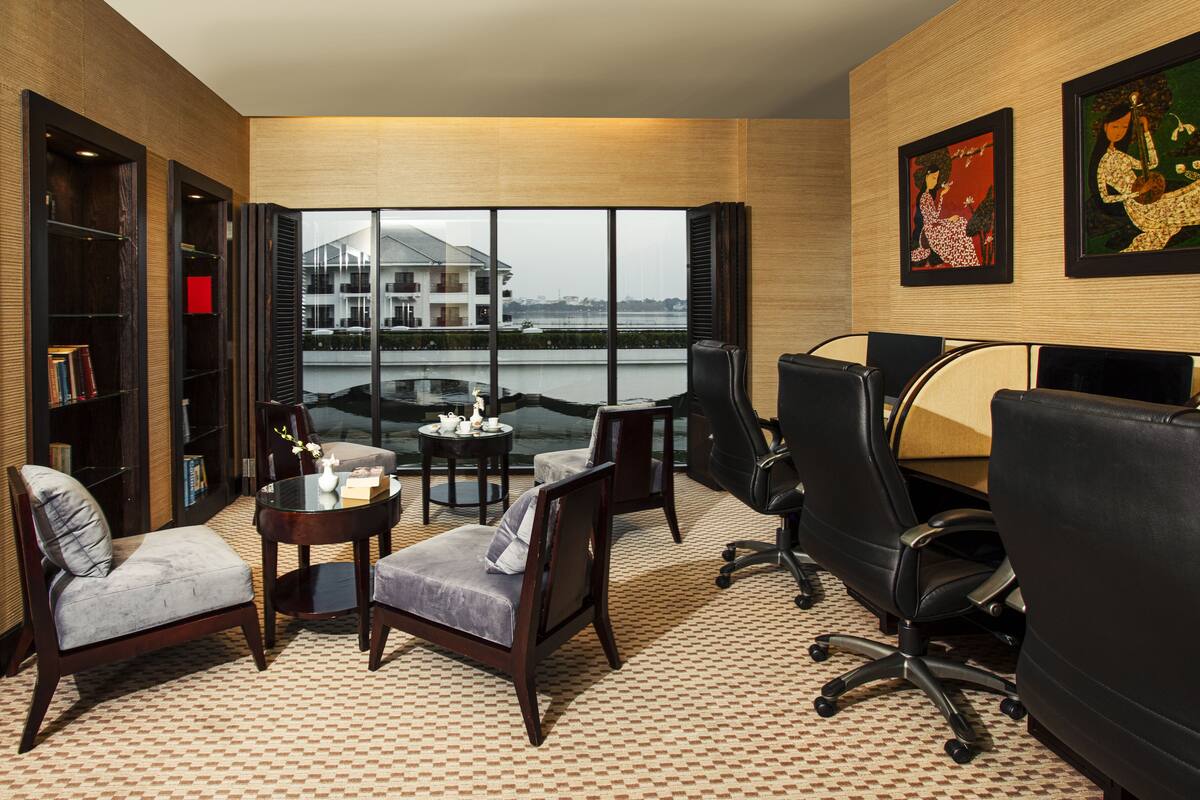 A modern office space with a view of a building across a body of water, featuring leather chairs, a small table with a teapot, and bookshelves.