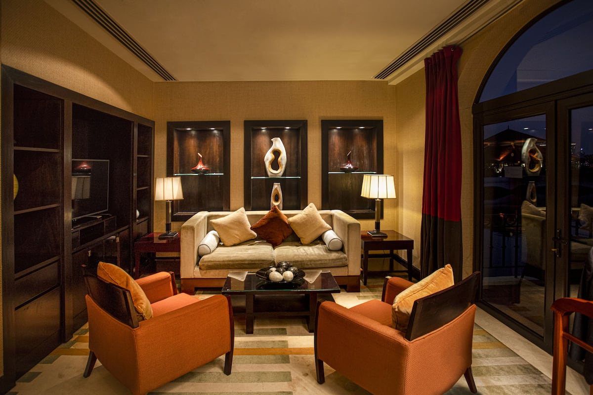 A modern living room with a sofa, two armchairs, a coffee table, and decorative items on shelves.
