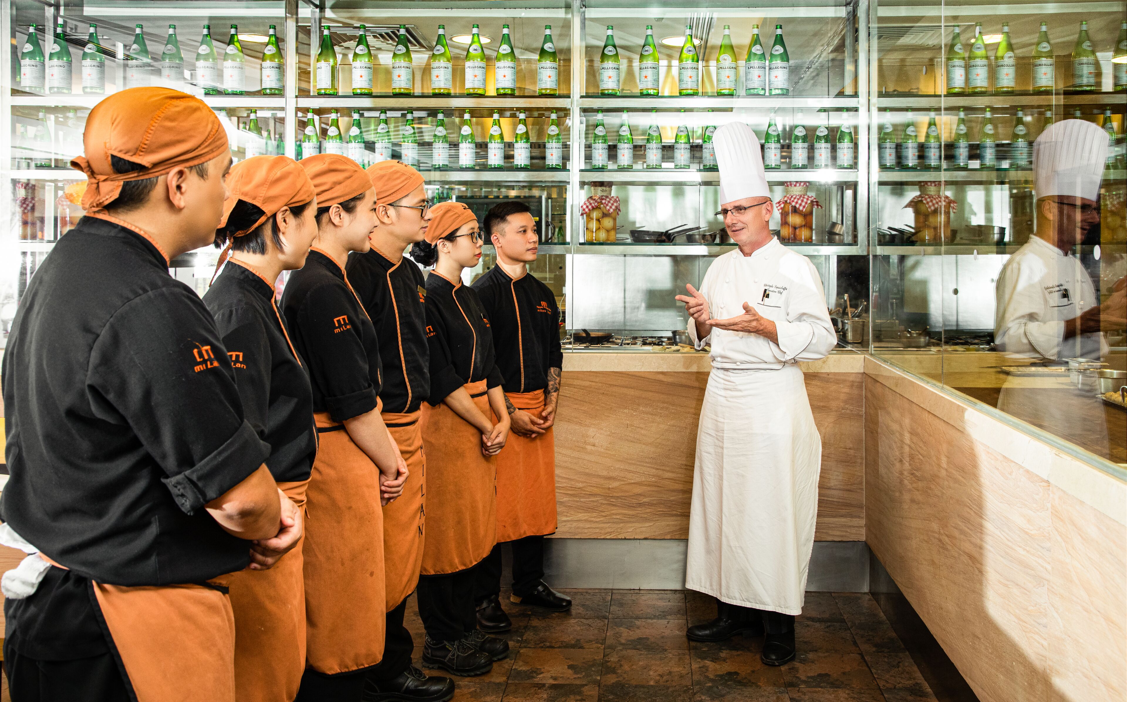 A chef instructing kitchen staff in a professional kitchen setting.