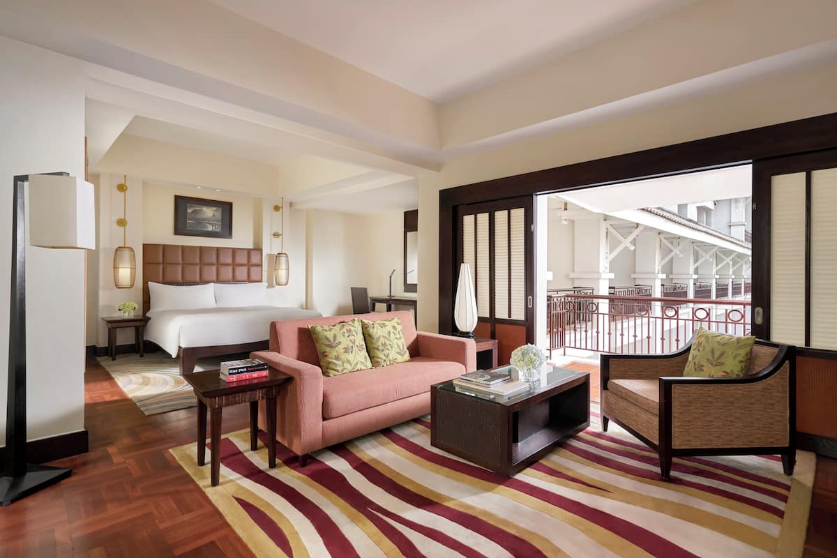 A hotel room with a bed, a pink sofa, a wooden coffee table, and a view of the outside balcony.