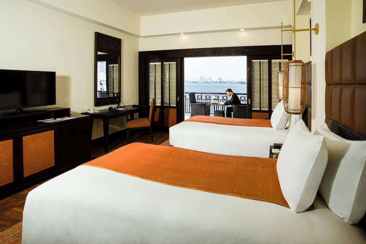 Een hotelkamer met twee bedden, een bureau, een televisie en uitzicht op de stad.
