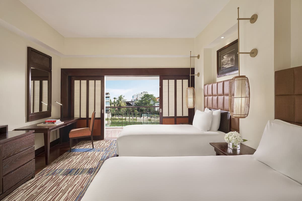 A hotel room with two beds, a desk, a chair, a large window, and a view of the outdoors.