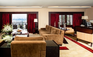 Een hotelkamer met een bank, fauteuil, eettafel en uitzicht op de stad door grote ramen.