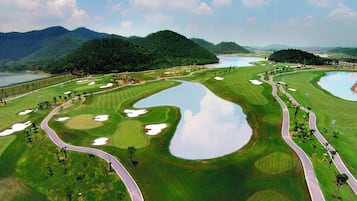 A golf course with multiple bunkers and water hazards, surrounded by lush greenery and mountains.