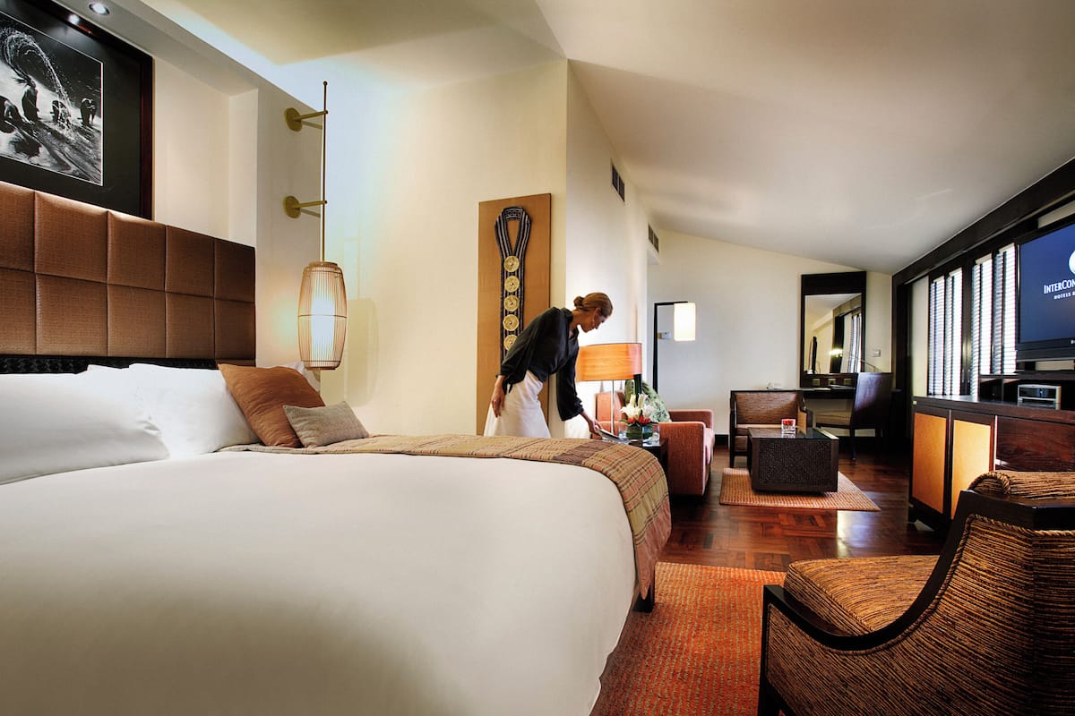 A hotel room with a large bed, a desk with a computer, a television, and a wall-mounted artwork.