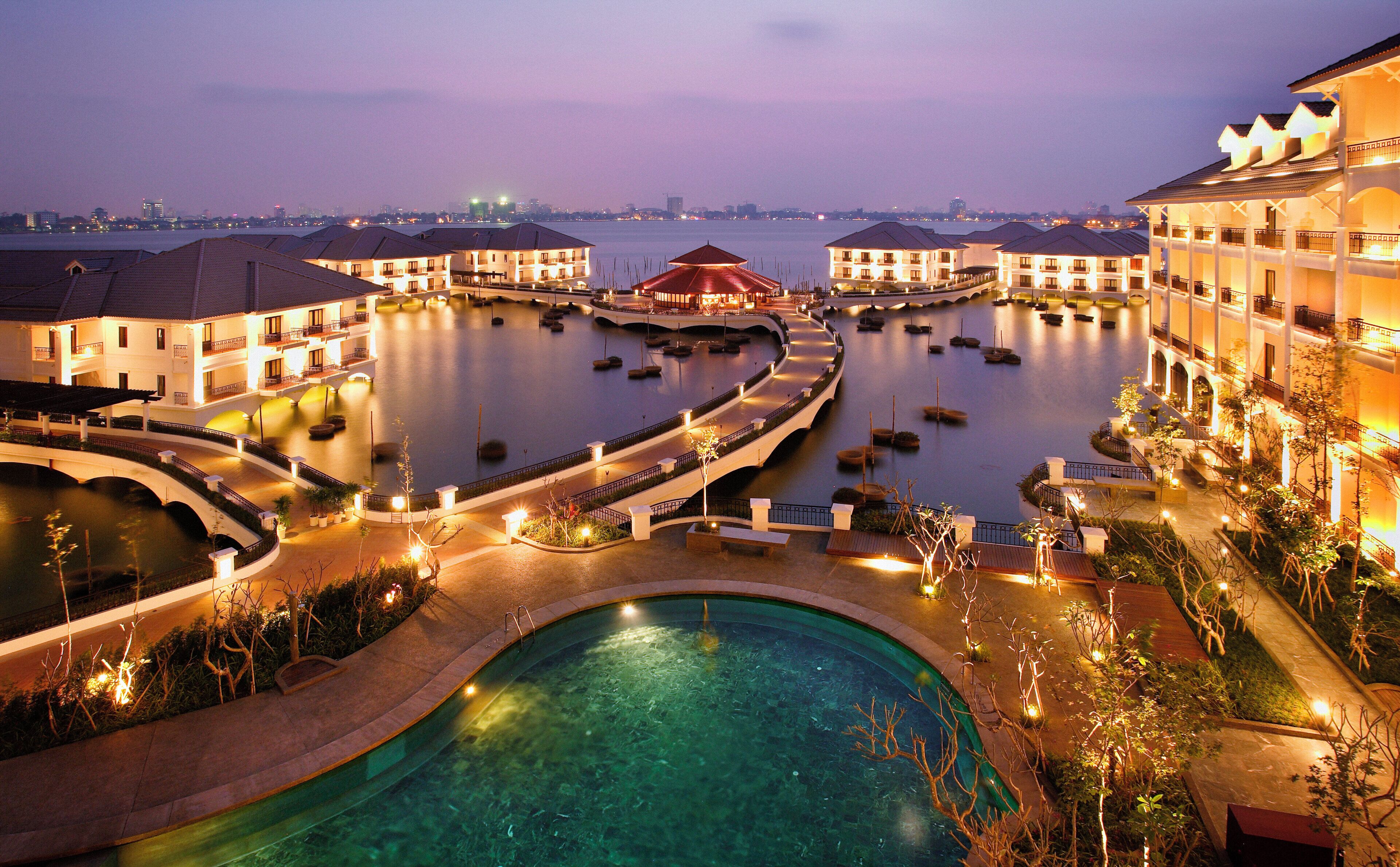 A hotel with a swimming pool, multiple connected water bodies, and a cityscape in the background.