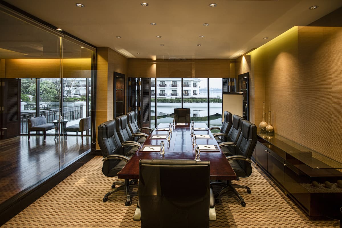 A conference room with a long table, multiple chairs, and a view through large windows.